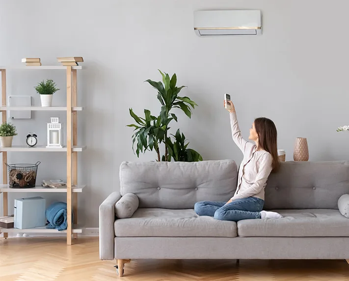 Woman on couch remote controlling AC unit.